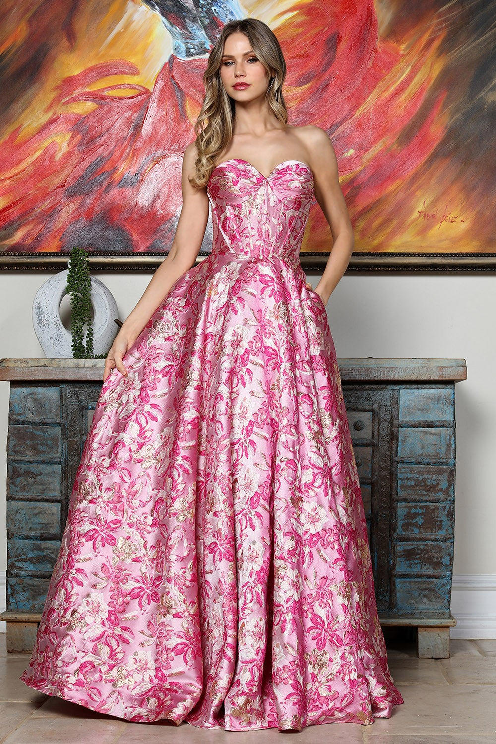 Woman in a pink floral dress standing in front of a colorful abstract painting.
